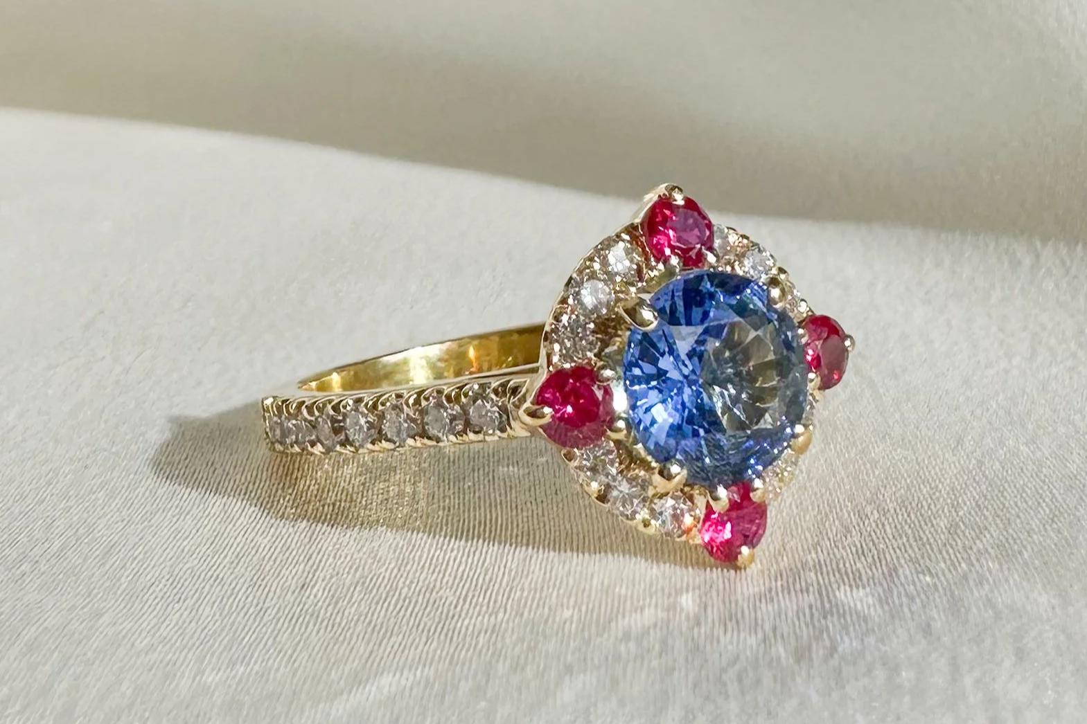 Katherine Elder Fine Jewellery bespoke cornflower blue sapphire ring with diamond halo and ruby accents yellow gold