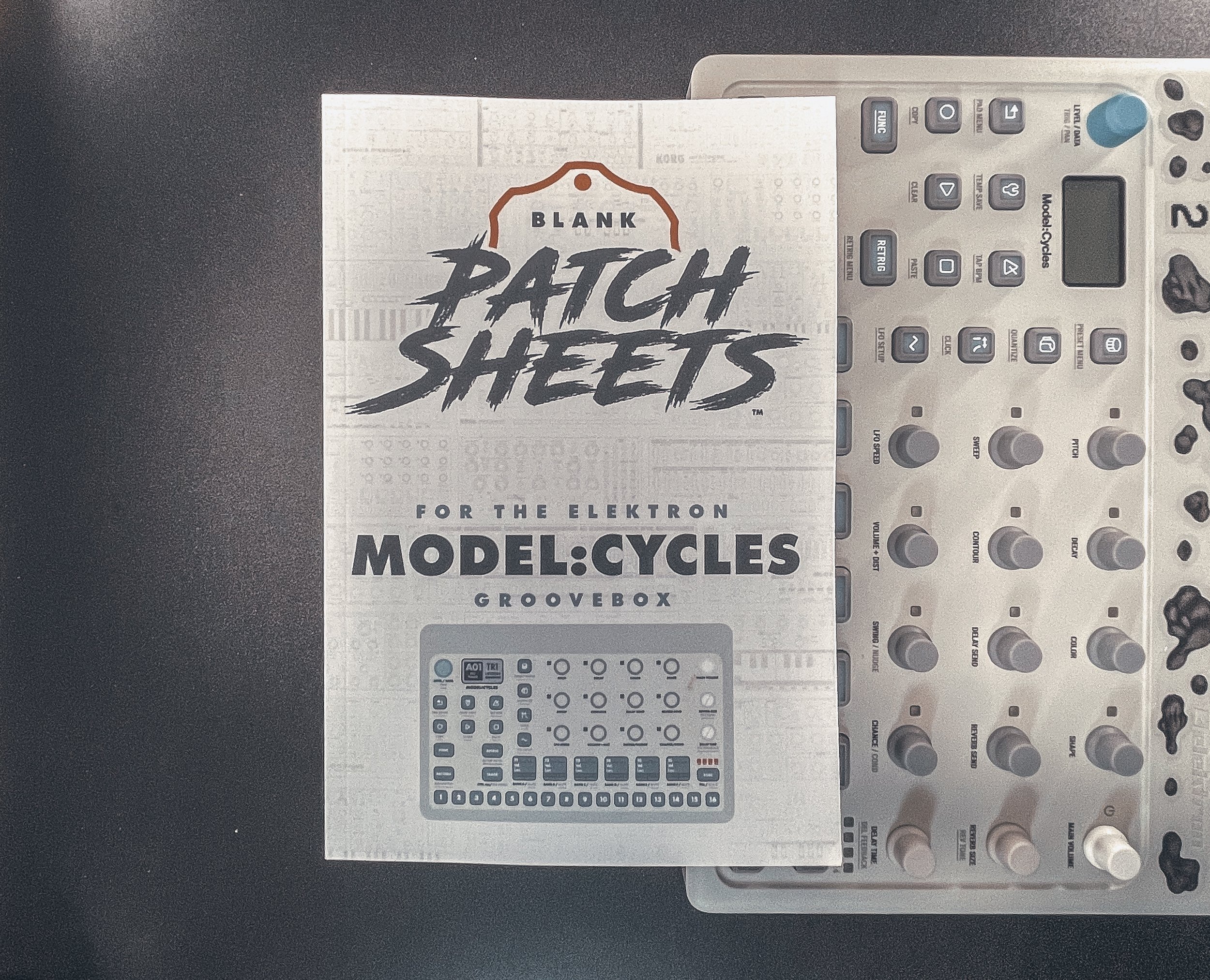A user manual titled 'Blank Patch Sheets for the Elektron Model:Cycles Groovebox' is placed on top of a music production device, the Elektron Model:Cycles groovebox, which has various knobs and buttons.