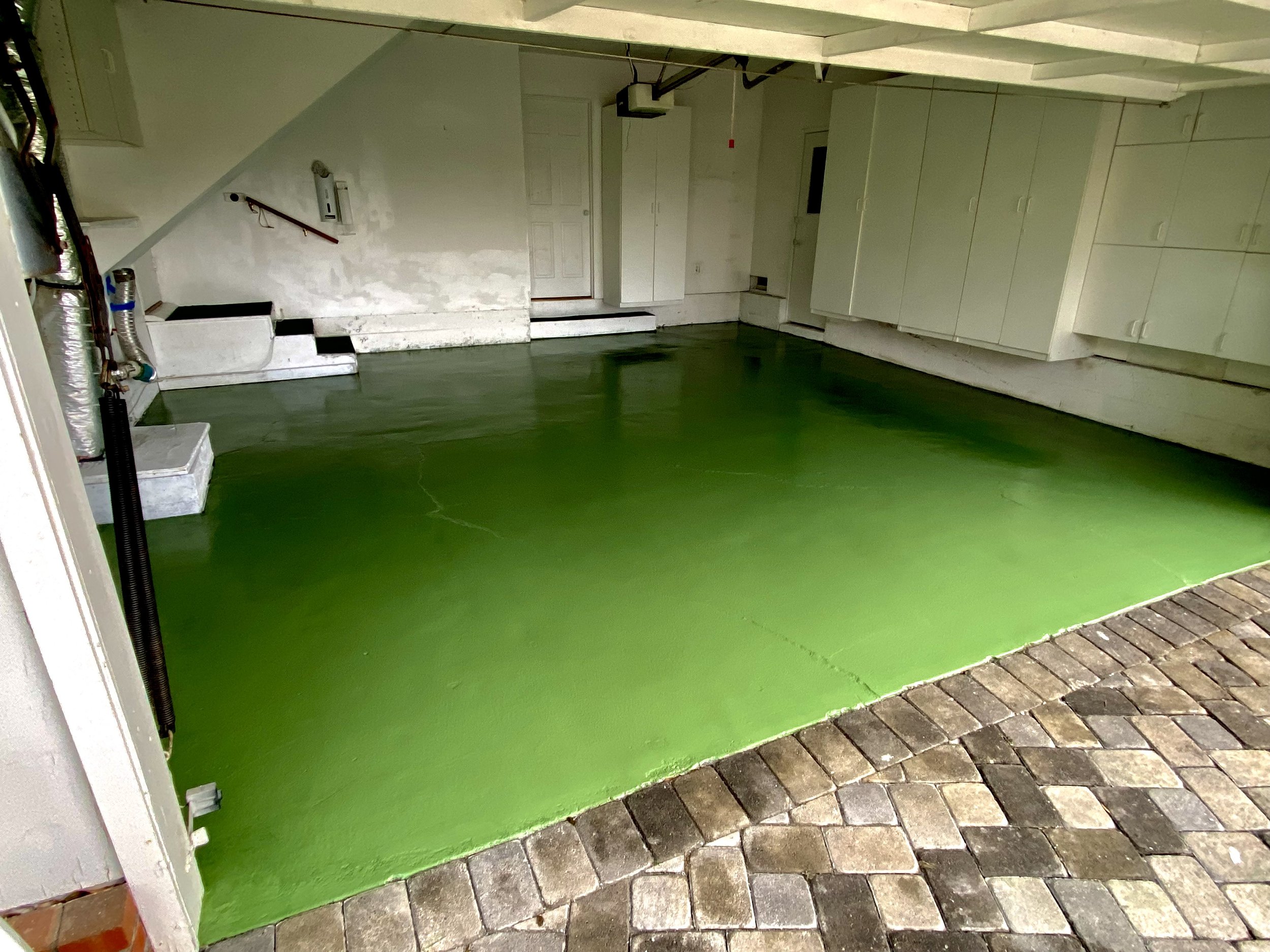 Clean white residential garage with bright green epoxy floor, built-in storage cabinets, steps, and a garage door opener.