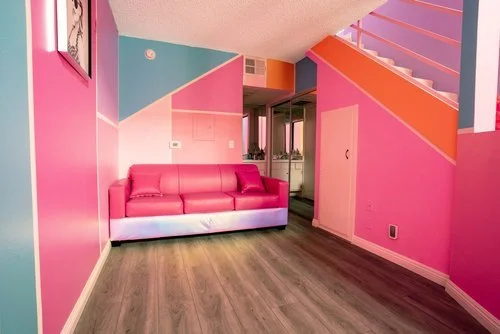 Colorful pink and orange living room with a red leather sofa, wood flooring, and staircase.