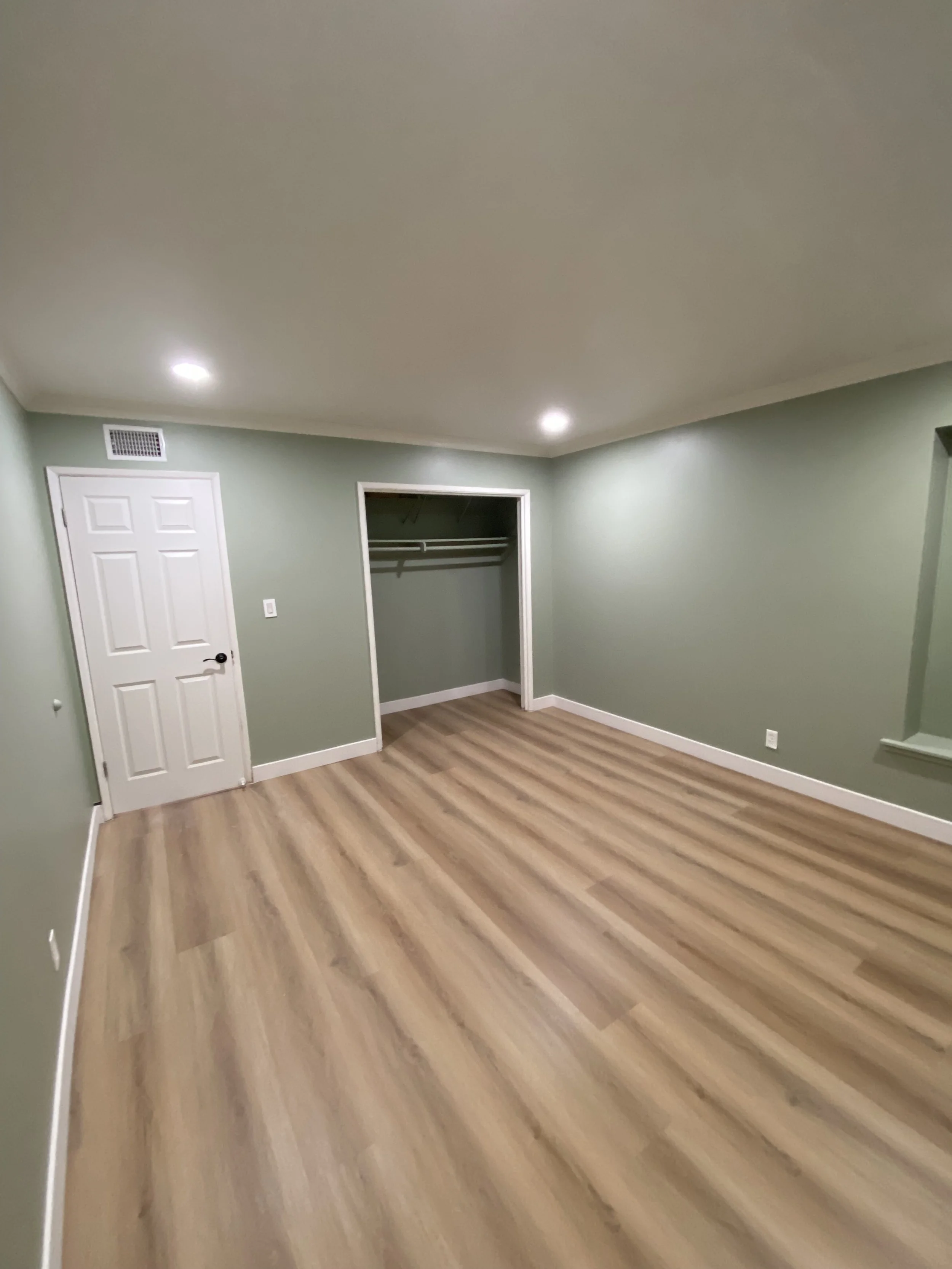 Empty green-painted room with recessed ceiling lights, white door, open closet, and wood-look flooring