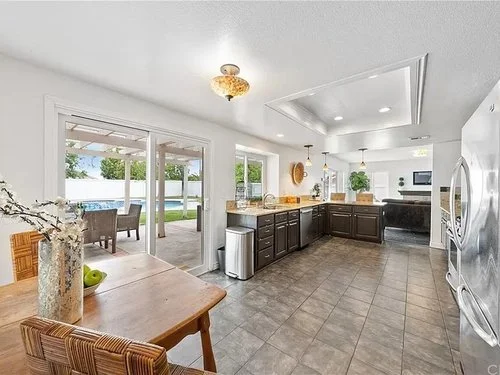 Bright modern kitchen with dark wood island, stainless steel appliances, dining table, and glass doors opening to a backyard pool