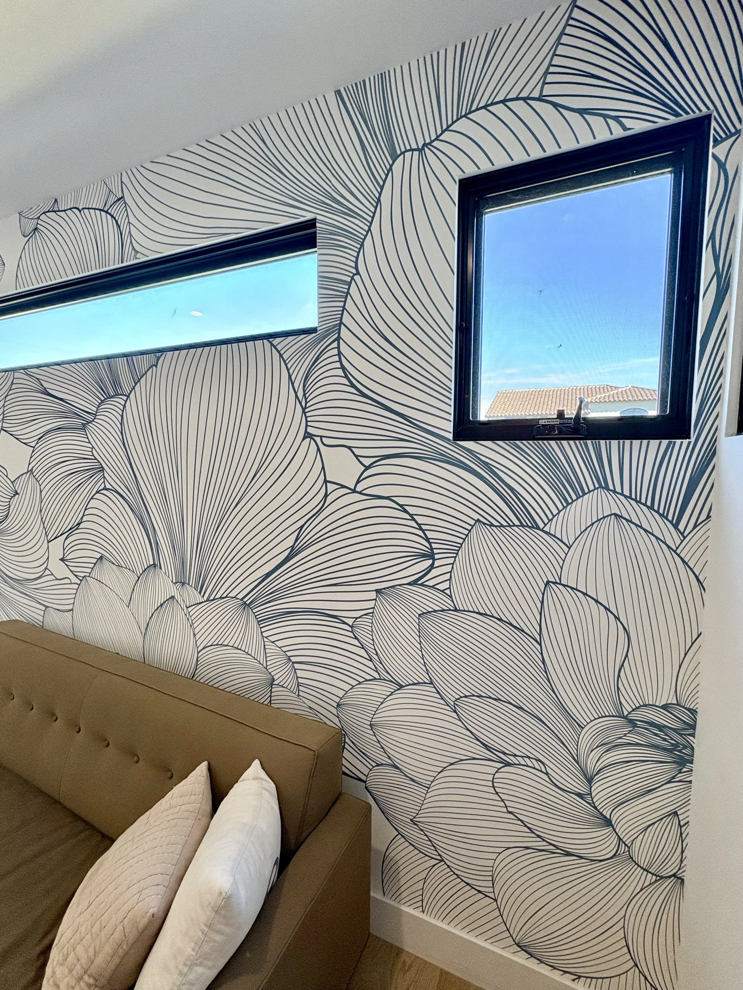 Bedroom with bold black-and-white botanical wallpaper, two windows, and a brown upholstered bed with white pillows.