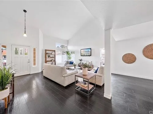 Bright modern open-plan living room with white sofas, dark hardwood floors, wall art, and woven baskets