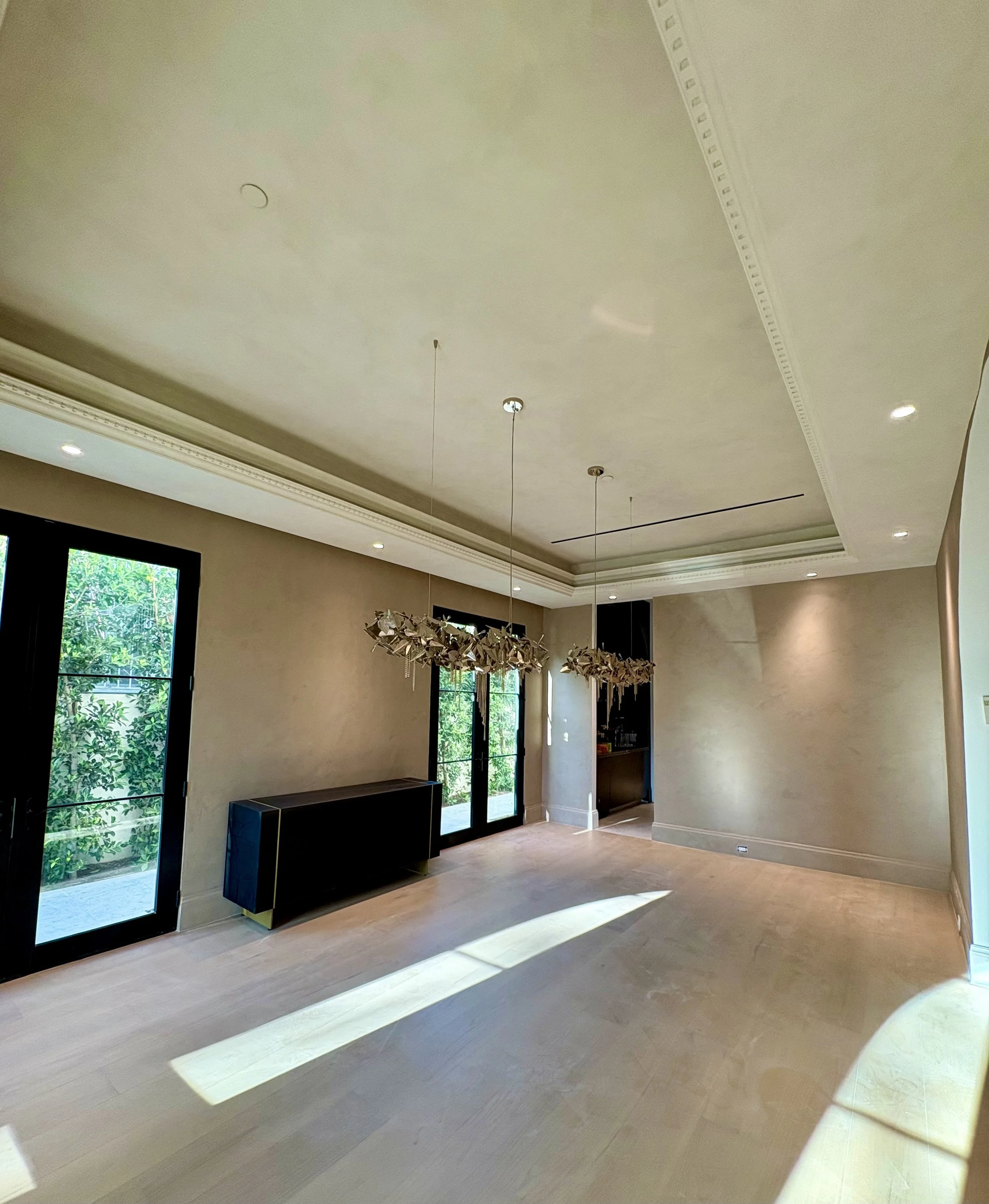 Taupe textured dining room walls with black-framed windows, sculptural chandelier, and dark console.