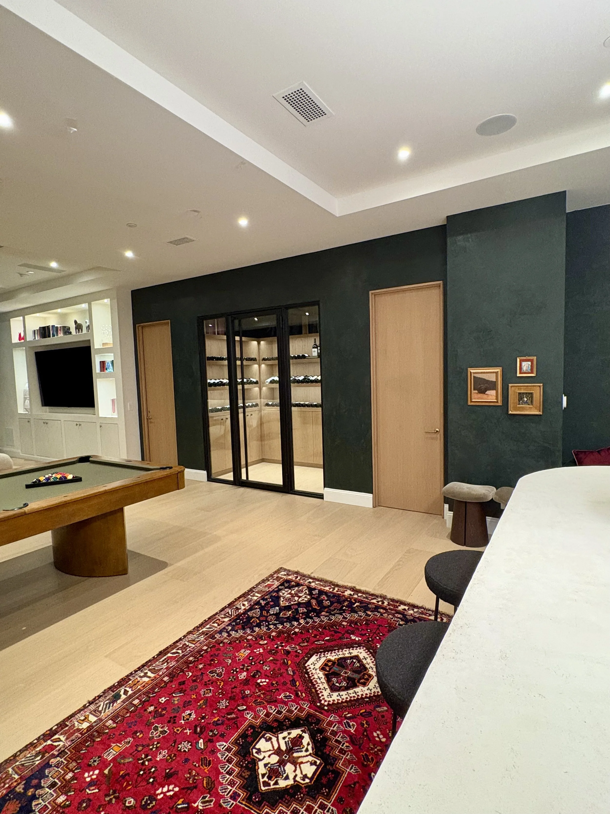 Dark green textured accent wall with natural wood door, framed artwork, and cream sofa in a modern interior.