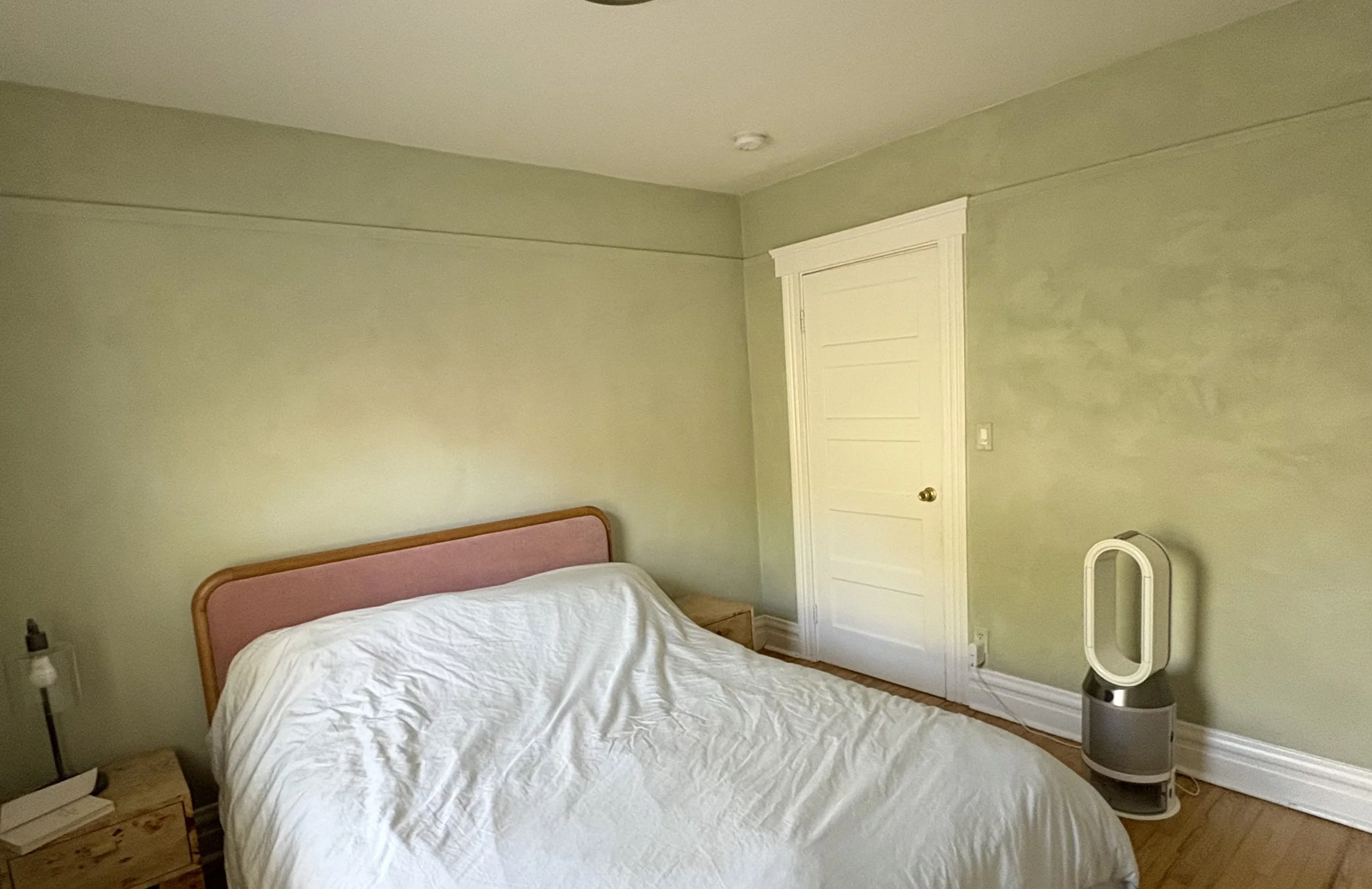 Bedroom with a pink upholstered bed, white bedding, green walls, a white door, nightstands, and a tower fan.