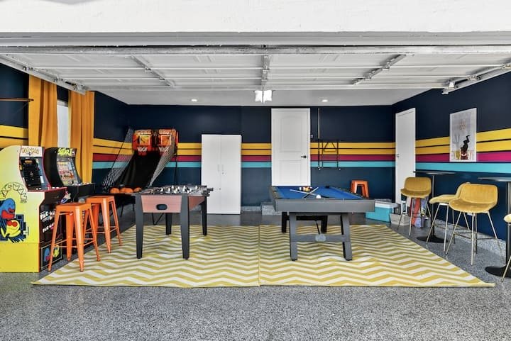 Colorful retro game room with arcade machines, foosball table, ping-pong table, bar stools, and striped walls