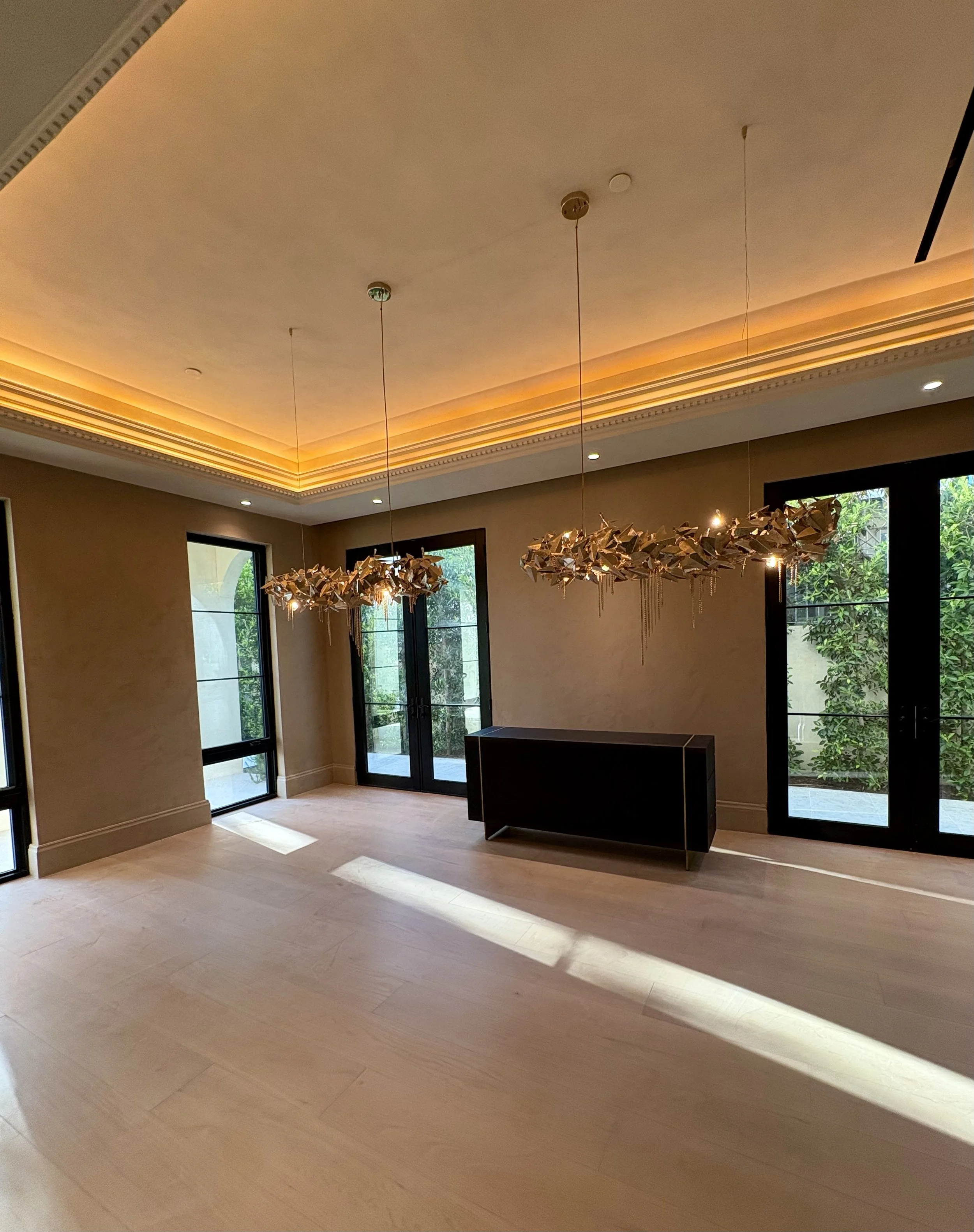 Elegant interior with ornate coffered ceiling, illuminated butterfly chandeliers, tall black-framed windows, and a dark console table.