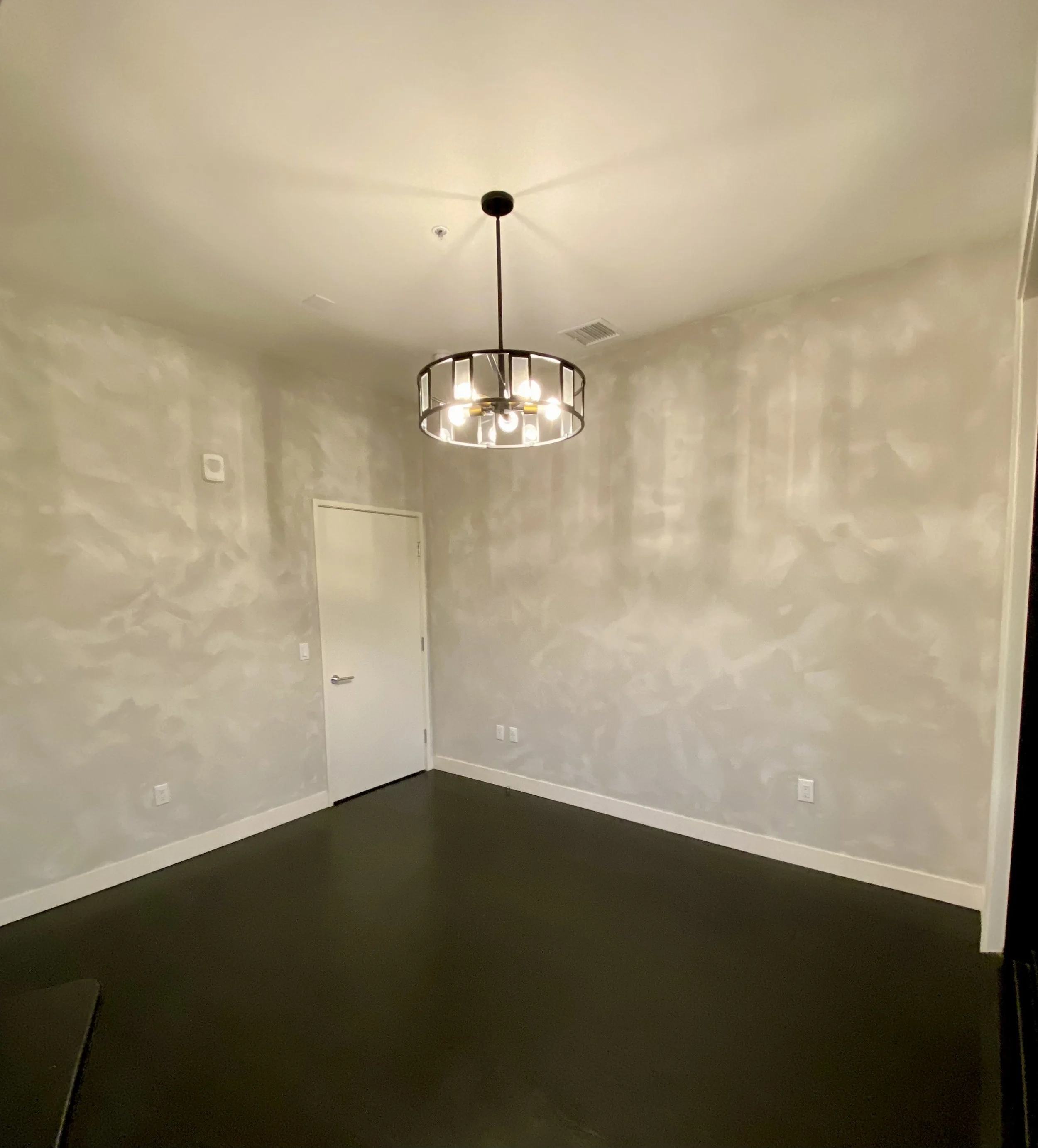 Empty room with gray textured walls, dark carpet, a white door, and a modern hanging light fixture.