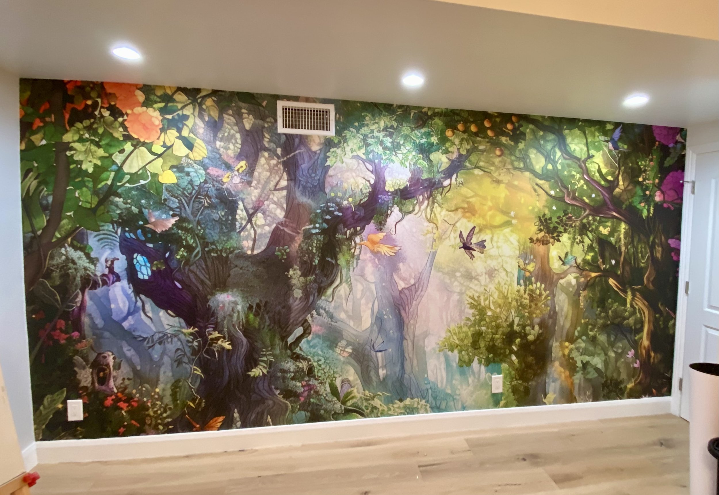 Whimsical enchanted forest mural with trees, flowers, birds, butterflies, and glowing woodland scenery on an interior wall