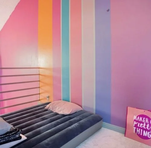 Colorful pastel-striped bedroom with a dark blue air mattress, pink pillow, window blinds, and pink inspirational sign