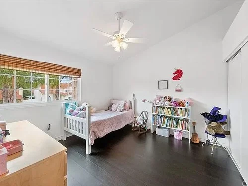 Bright children’s bedroom with a crib, twin bed, bookshelf, rocking chair, ceiling fan, and large window