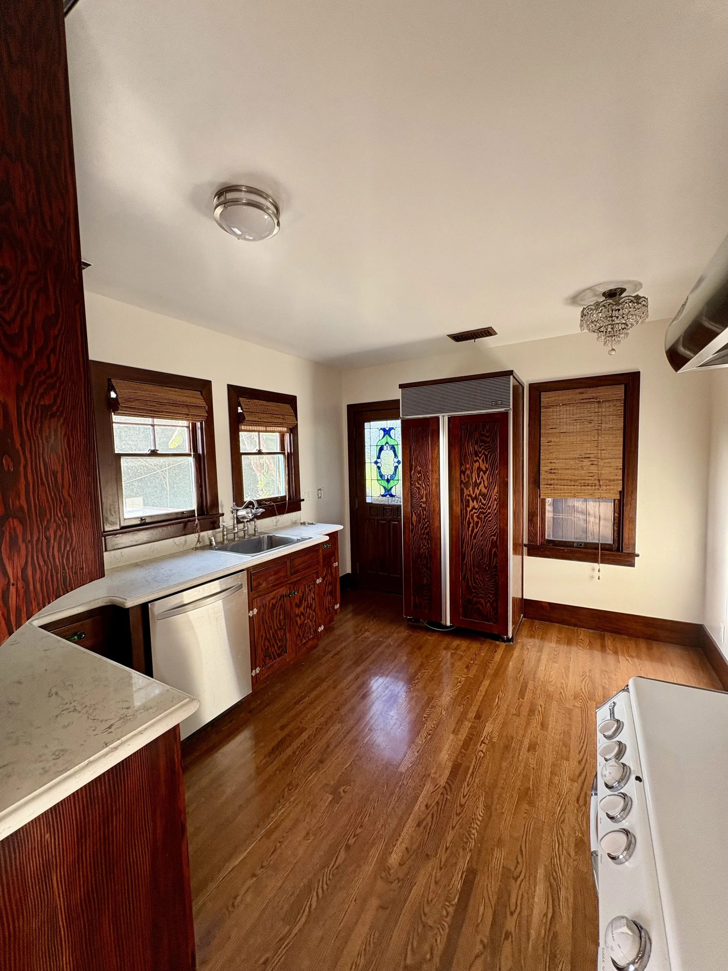 Vintage kitchen with dark wood cabinets, marble countertops, farmhouse sink, stainless refrigerator, hardwood floors, bamboo blinds, and a crystal ceiling light