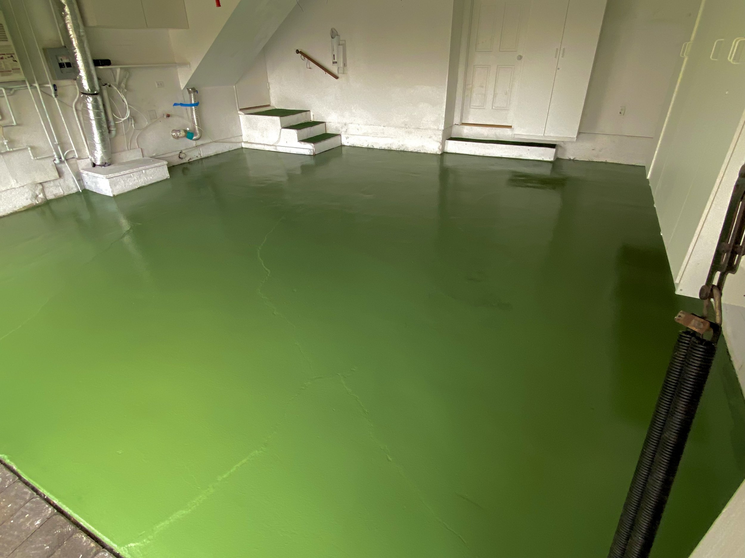 Finished basement with bright green epoxy floor, utility pipes, stairs, and doors