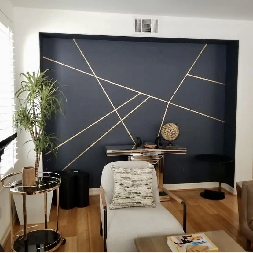 Modern living room with navy geometric accent wall, white lounge chair, console table, plants, and round side tables
