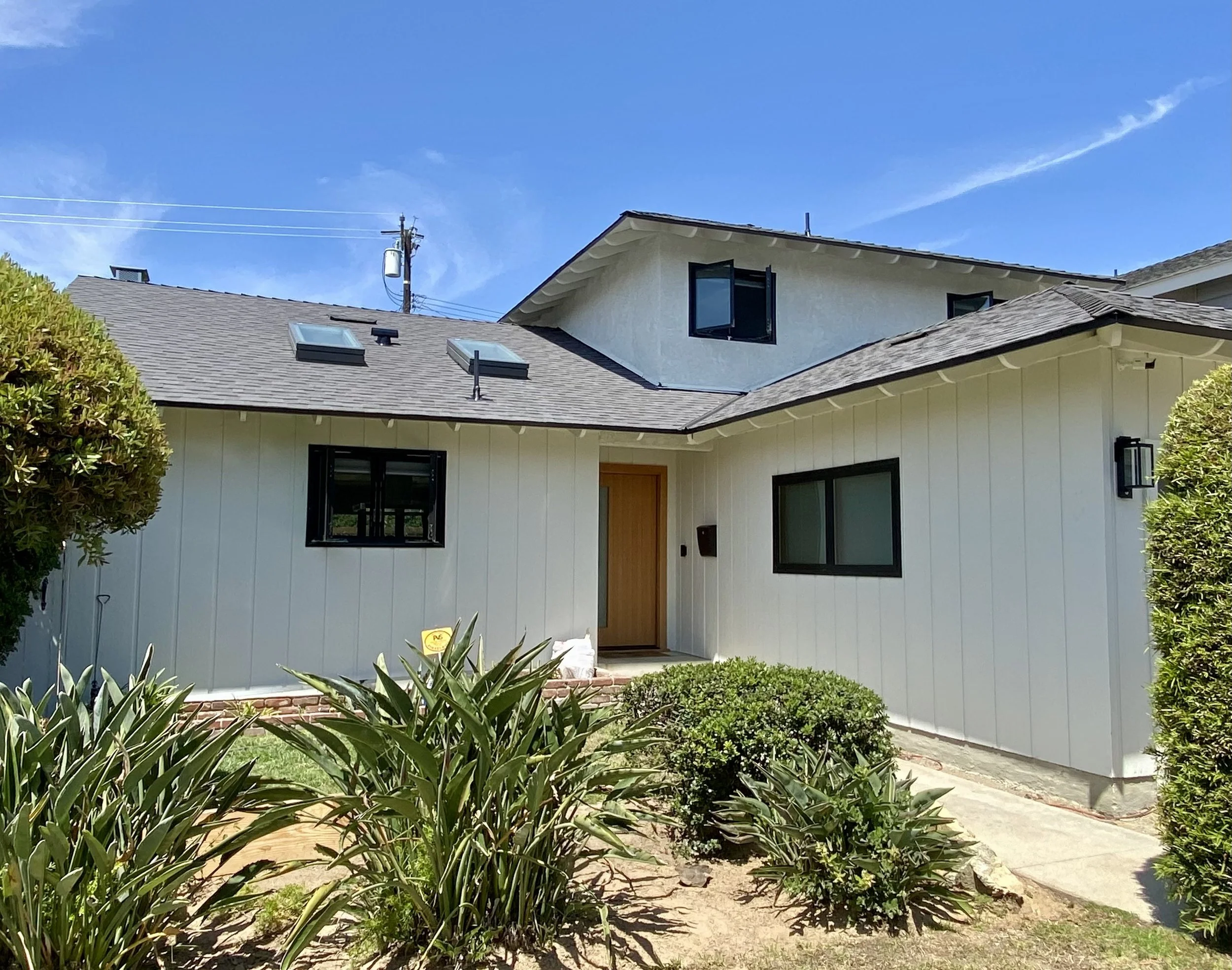 White modern single-story home with black-trimmed windows, skylights, landscaped front yard, and a sunny blue sky