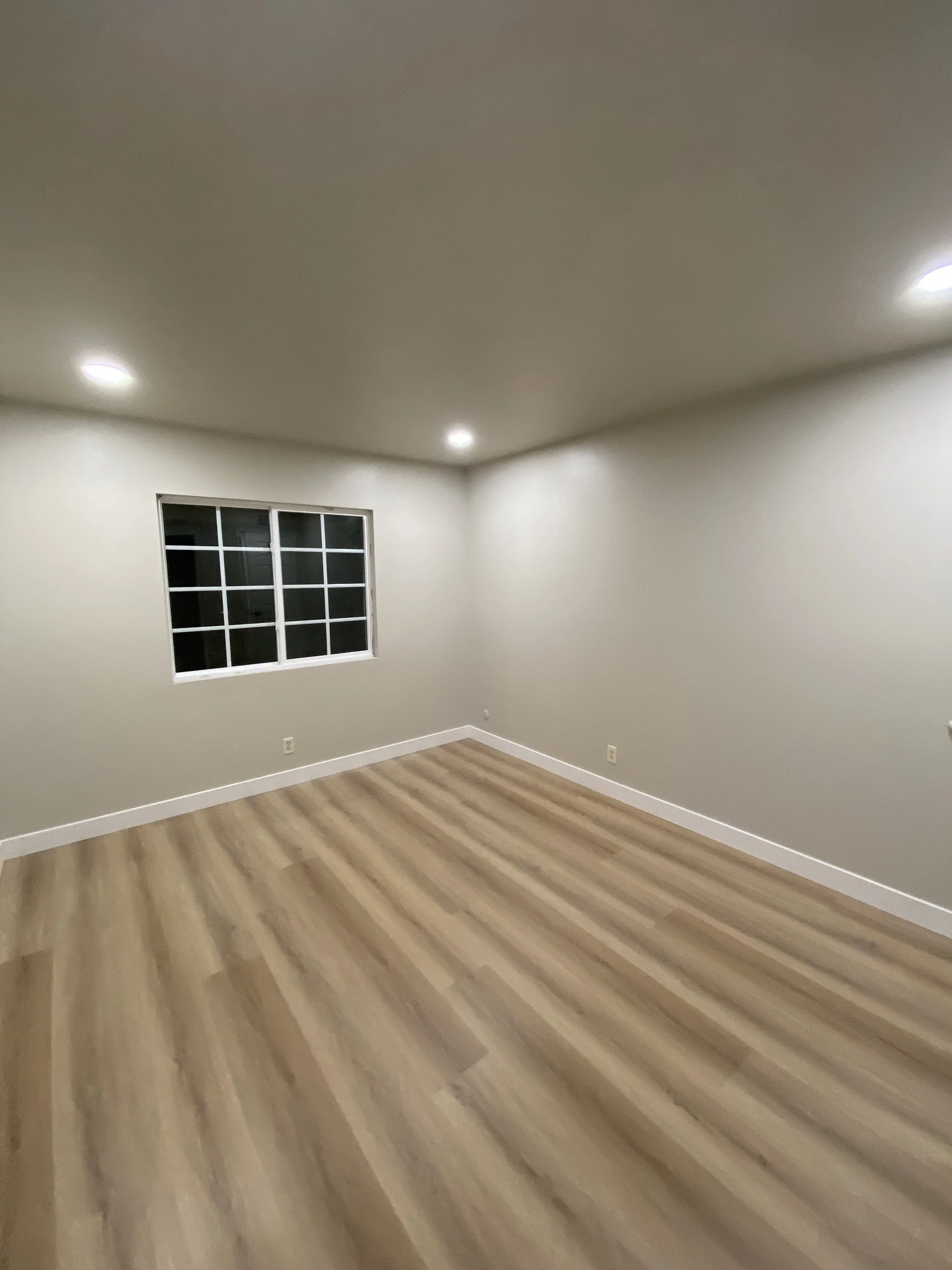 Empty room with gray walls, recessed ceiling lights, a gridded window, white trim, and light wood flooring.