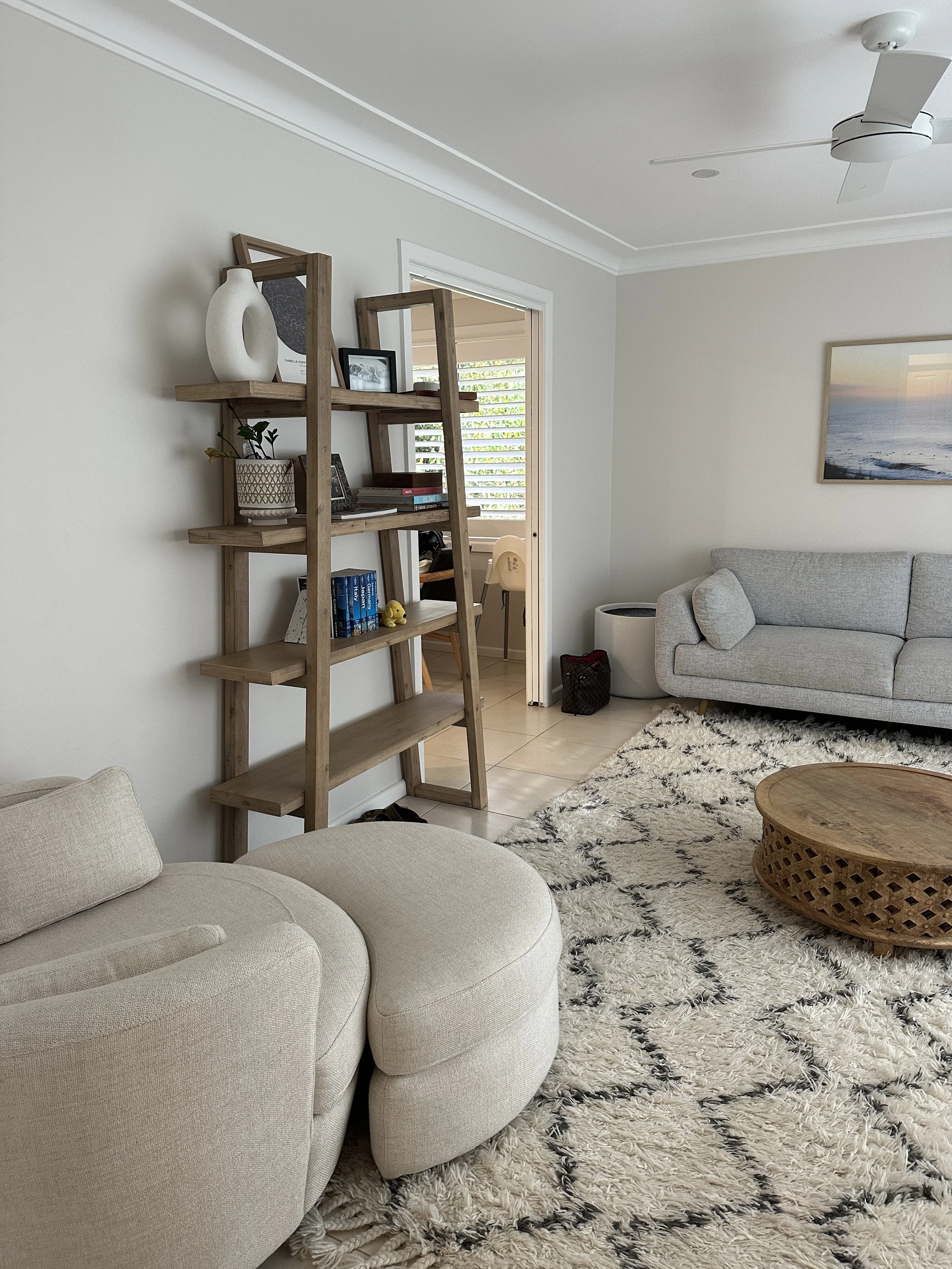 Living room with beige and gray sofas, a wooden coffee table, a patterned rug, a wooden bookshelf, and a ceiling fan.