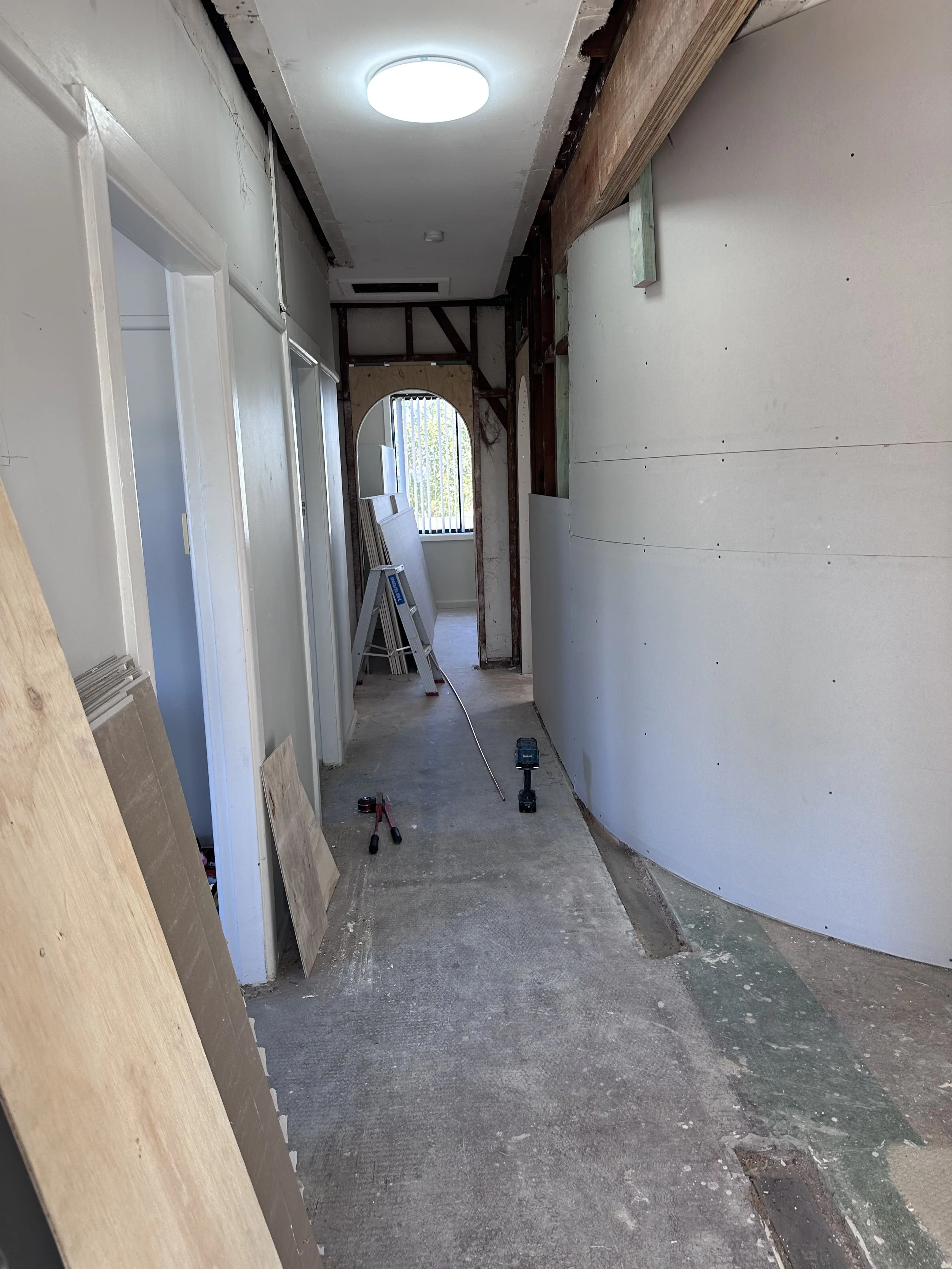 Interior of a room under renovation with partially finished walls, construction tools on the floor, and boards leaning against the wall.