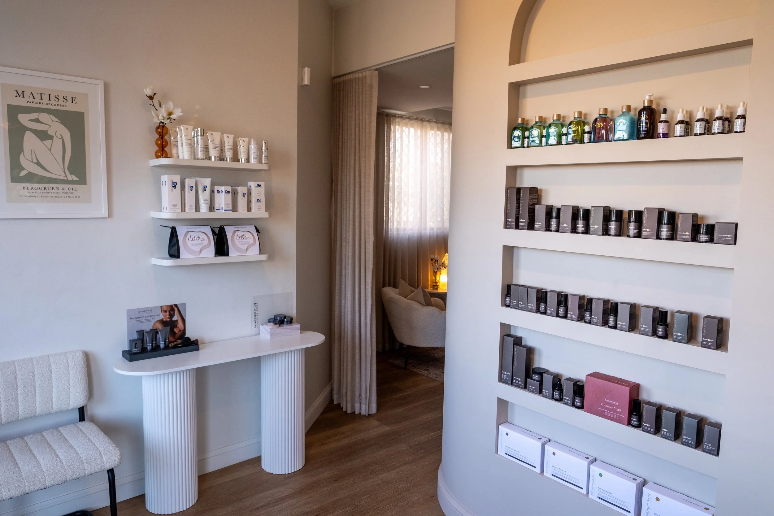 Commercial Interior styling & design in Sydney, New South Wales, of a spa or beauty salon with shelves of skincare products, a small table, a chair, and a cozy seating area with curtains and a lamp