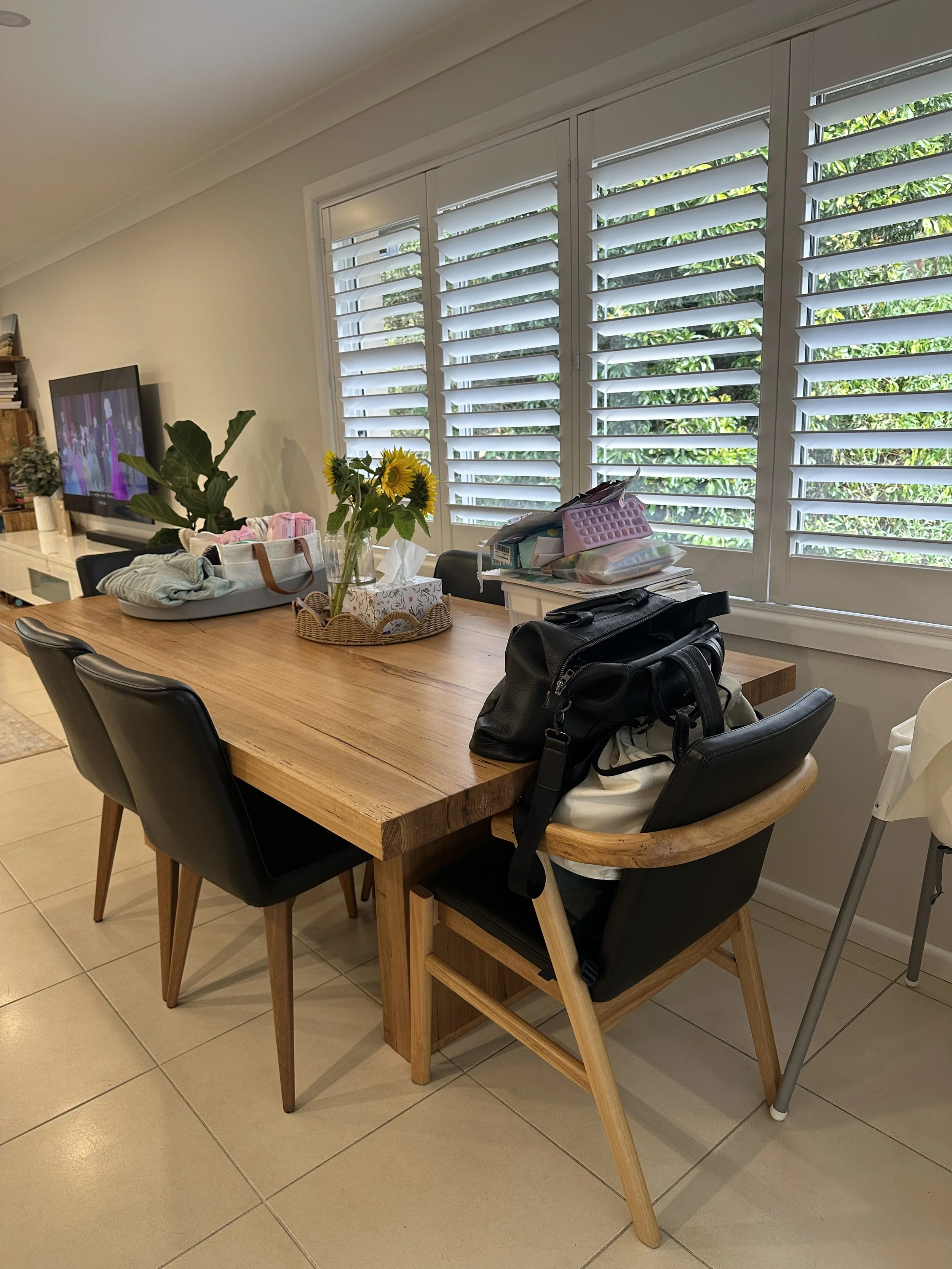 A dining table in a room with a window and shutters, decorated with sunflowers and various items, including bags and paper tissues.