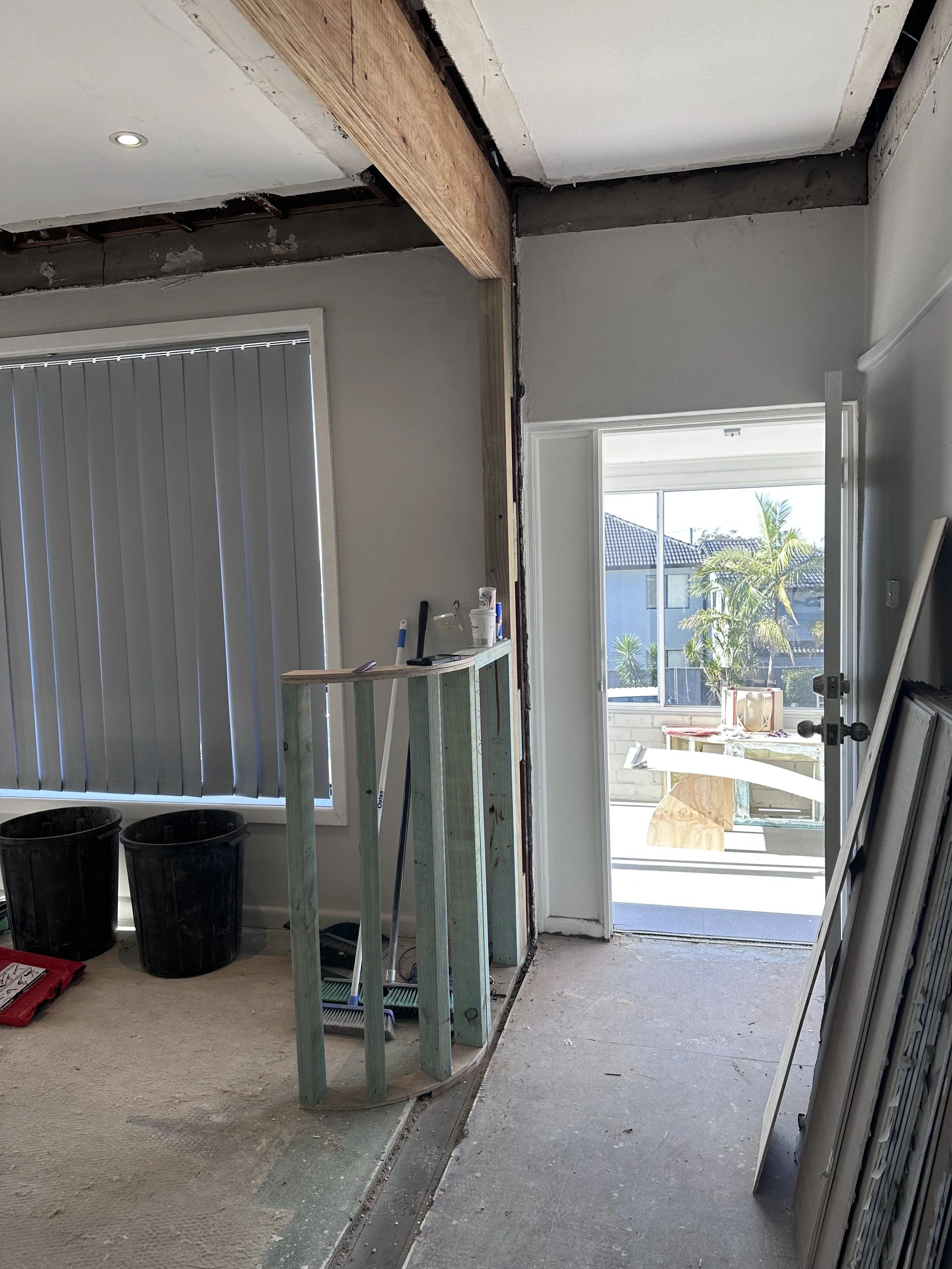 Room undergoing renovation with exposed framework, partially removed wall, and construction tools and materials.
