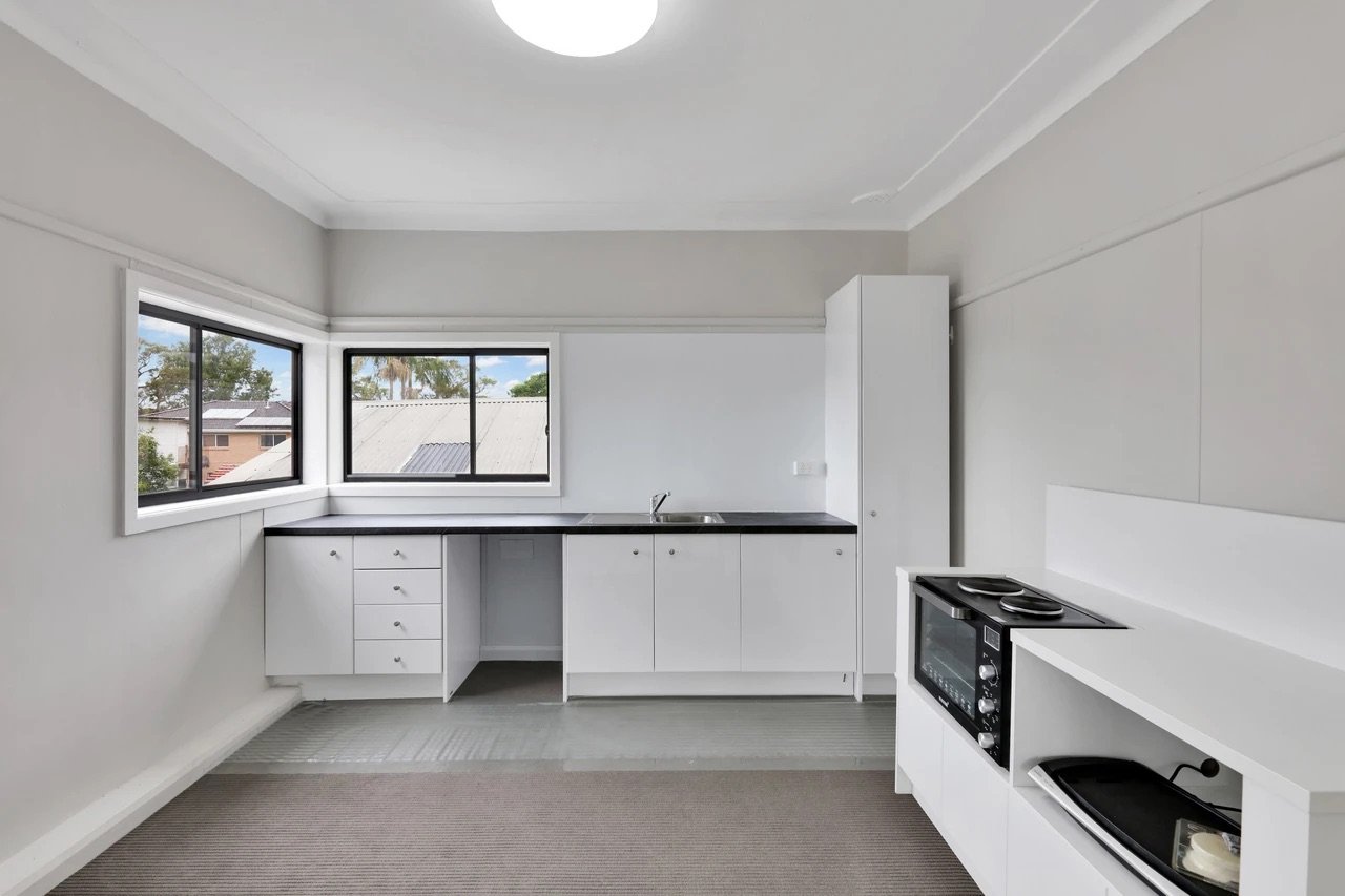 Empty kitchen with white cabinets, black countertop, double window, stove, and microwave.