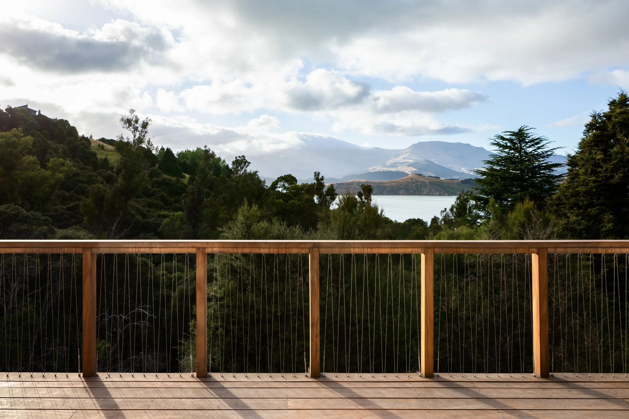 Timber deck with slender wire balustrade overlooking native vegetation, Lyttelton Harbour and the surrounding Port Hills.