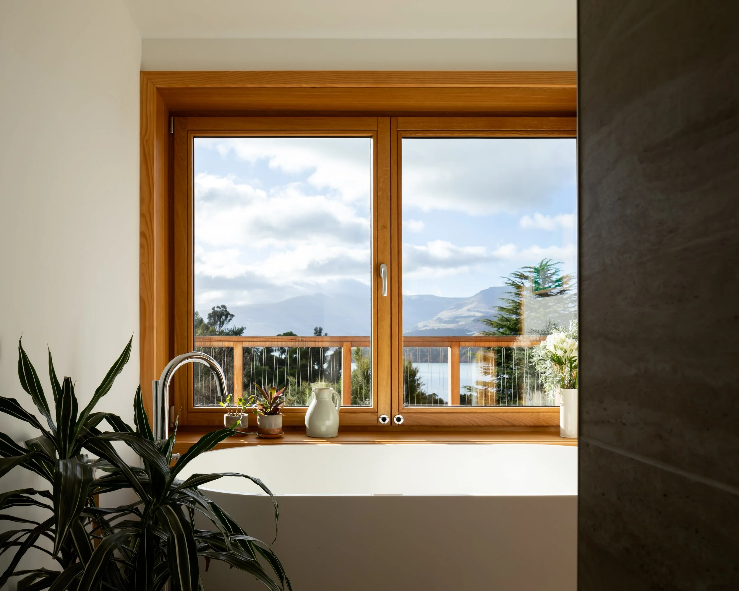 Bathroom window framed in timber overlooking Lyttelton Harbour and the surrounding hills.