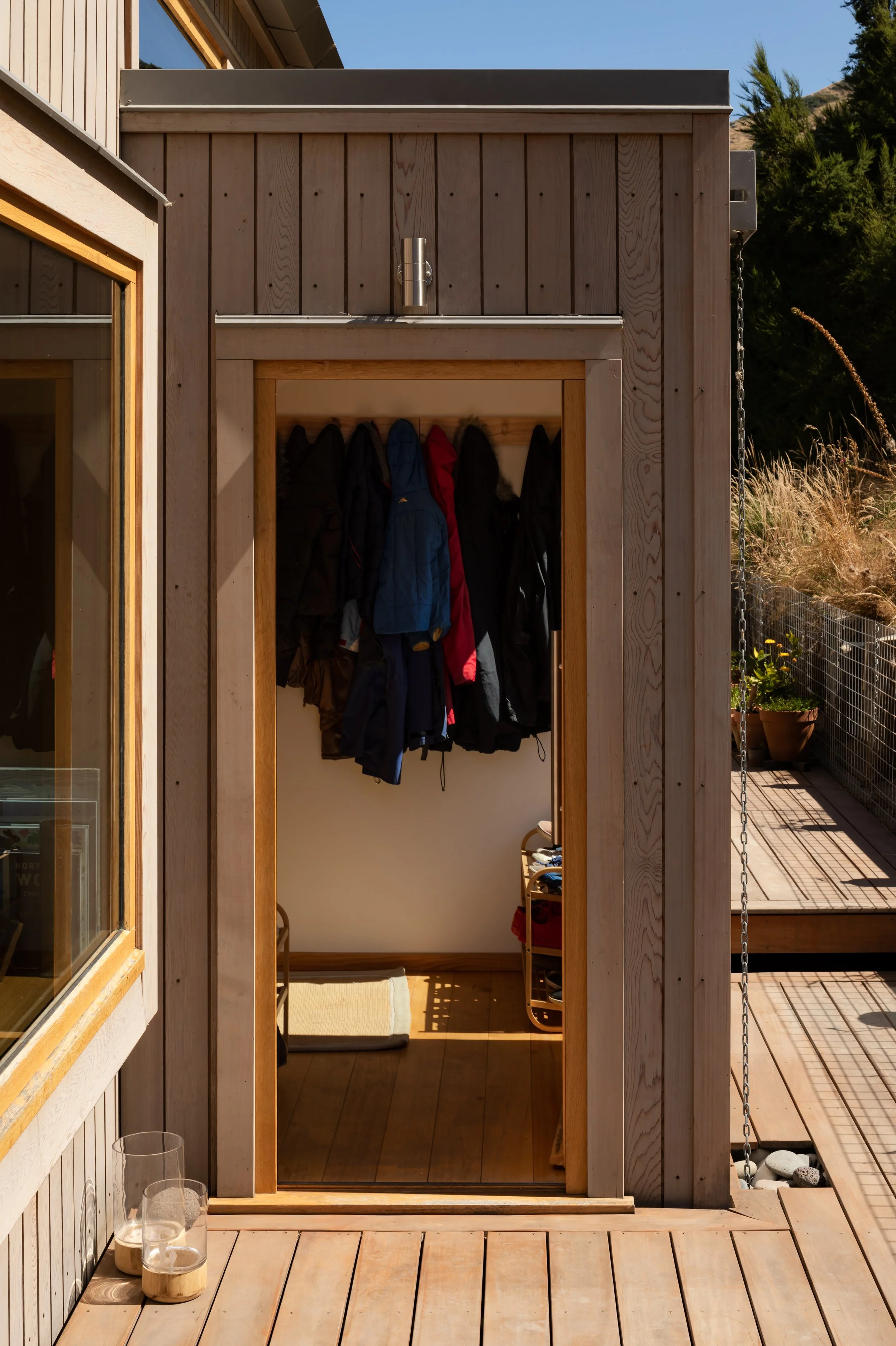 Timber-clad entrance and utility space opening onto a raised timber deck, with coats stored inside.