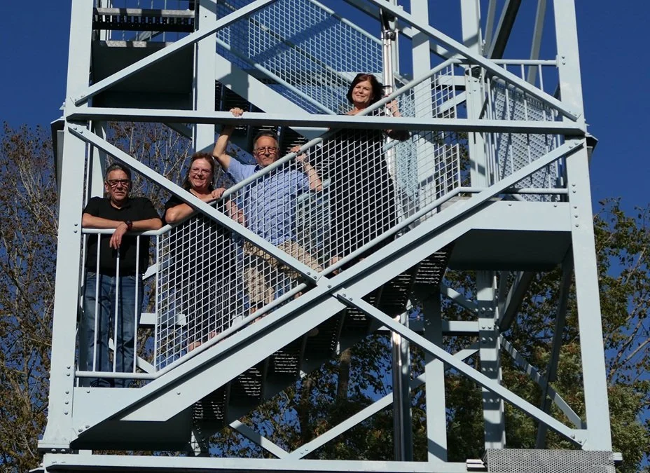 auf der Treppe eines Turmes sind 4 Erwachsene, die sich lächelnd über das Geländer hängen
