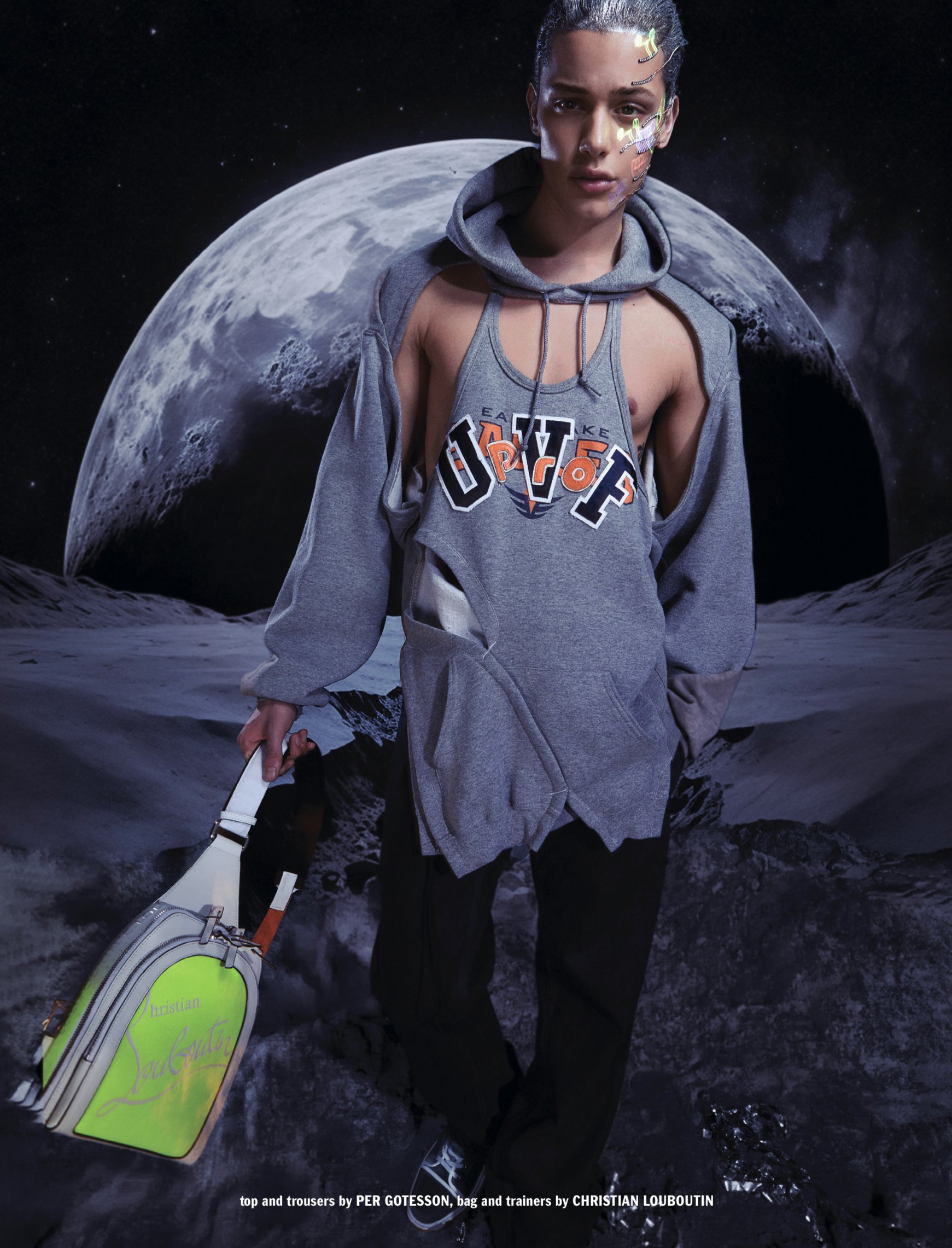 A model in a torn hoodie stands in front of a moon backdrop while holding a designer bag.