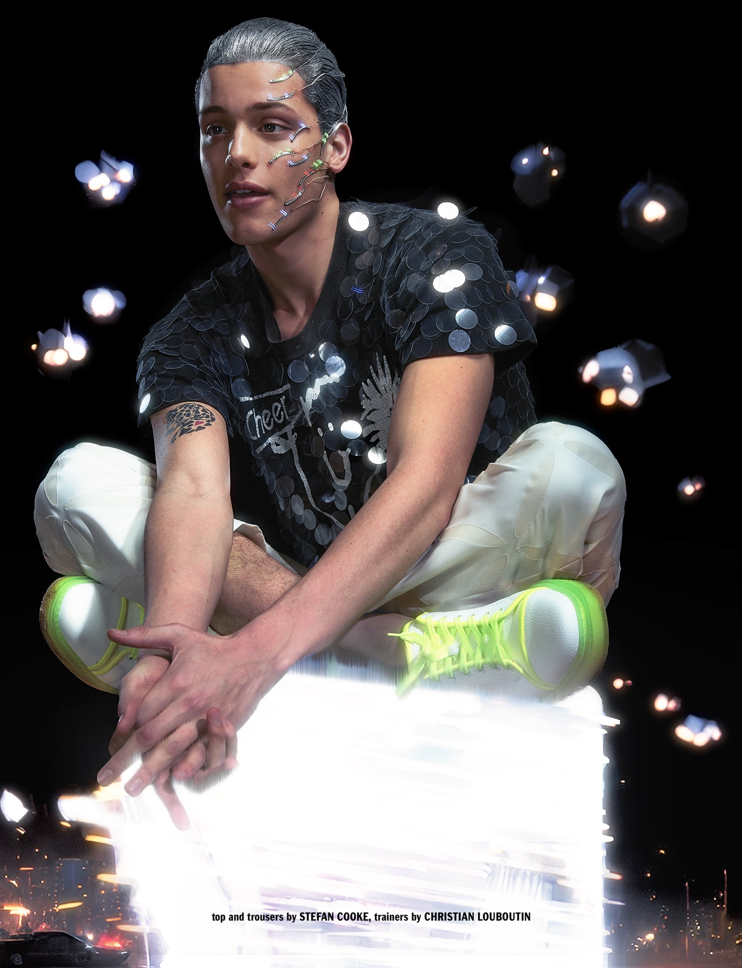 A person with silver hair and decorative face pins wearing a black sequin shirt, white pants, and neon green sneakers by Christian Louboutin. The background is dark with bright abstract lights.