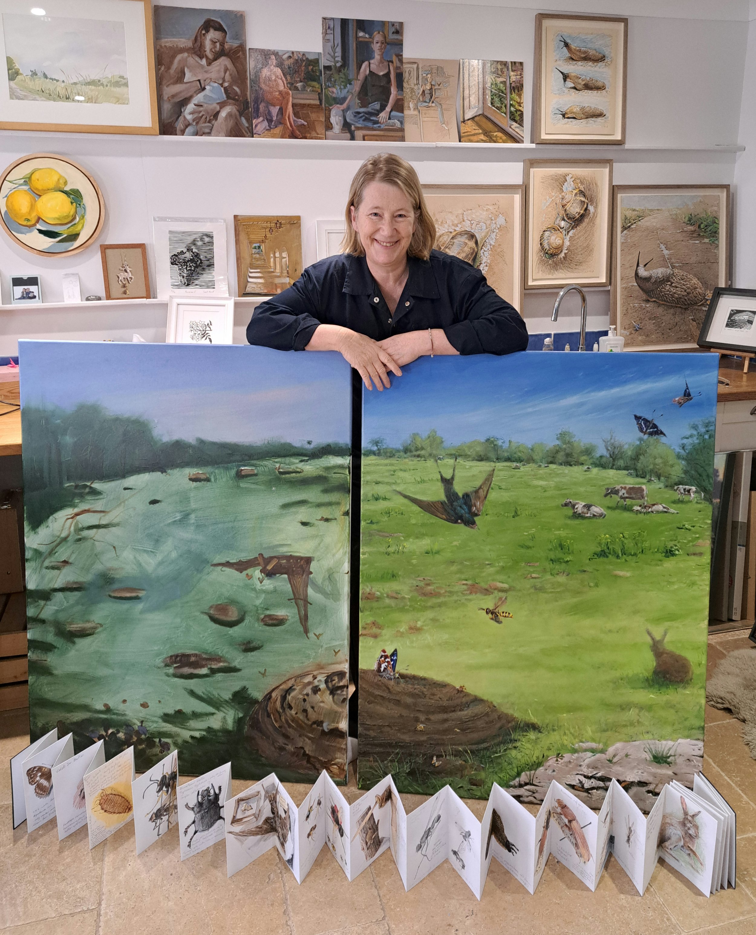 Gail standing behind two unfinished canvases, with a concertina sketchbook open on the floor