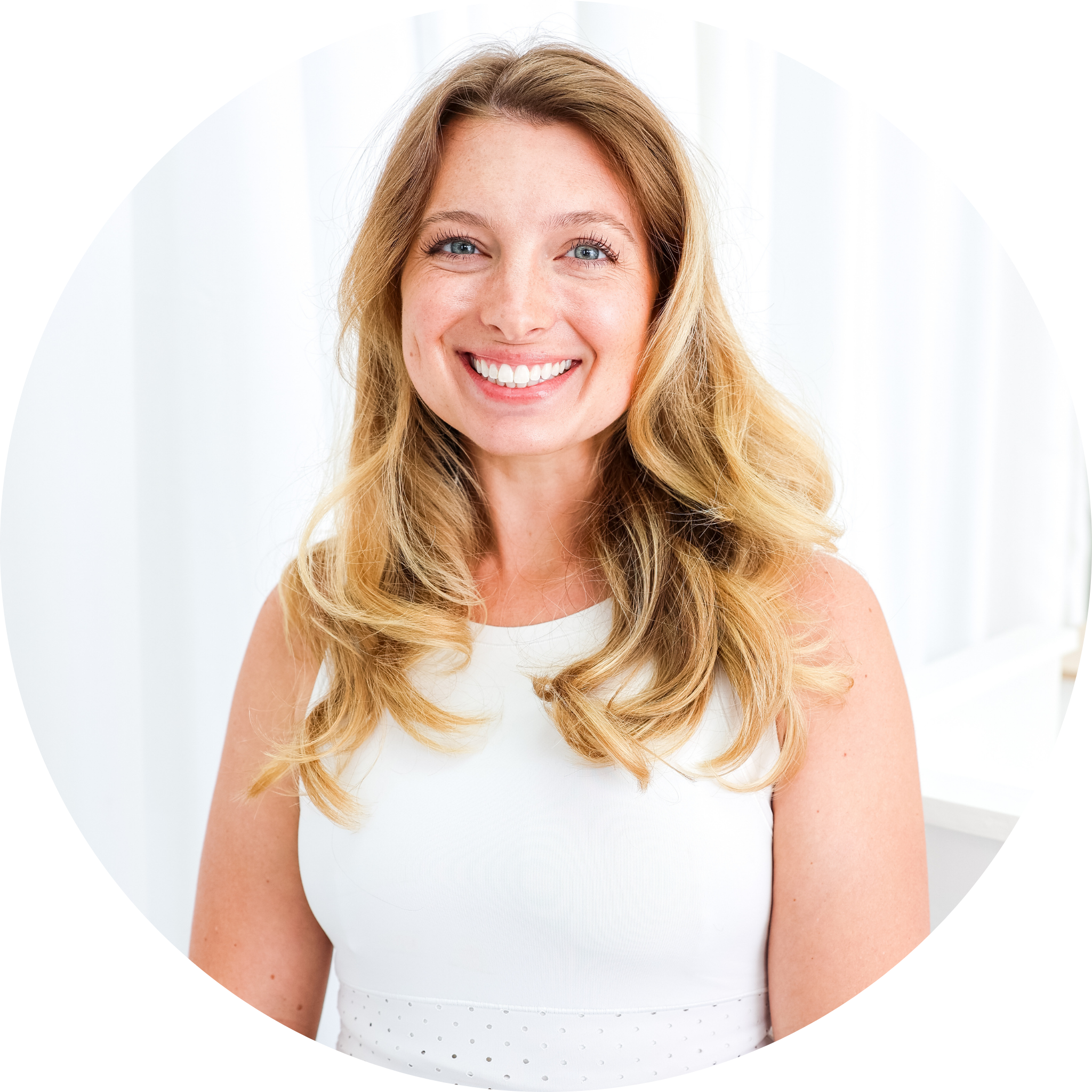 Smiling woman with long blonde hair wearing a light blue sports top and black leggings, leaning on a white surface in a bright indoor setting.