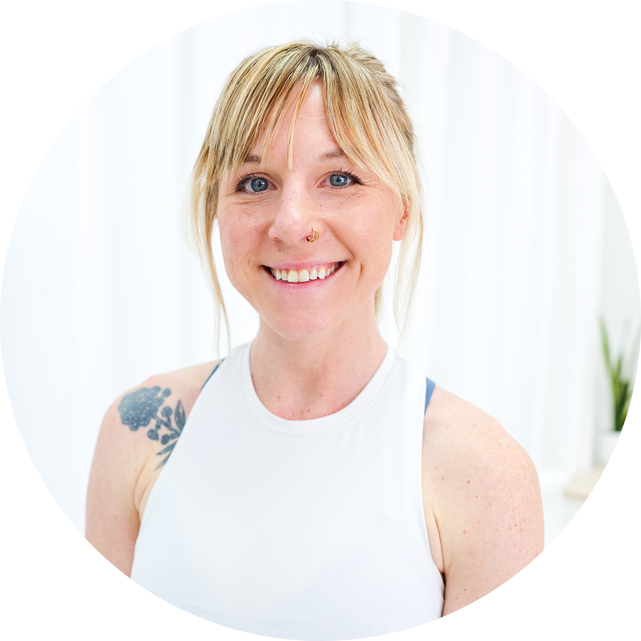 A young woman with long, light brown hair, freckles, and a septum piercing, wearing a beige spaghetti strap top, smiling at the camera against a plain white background.