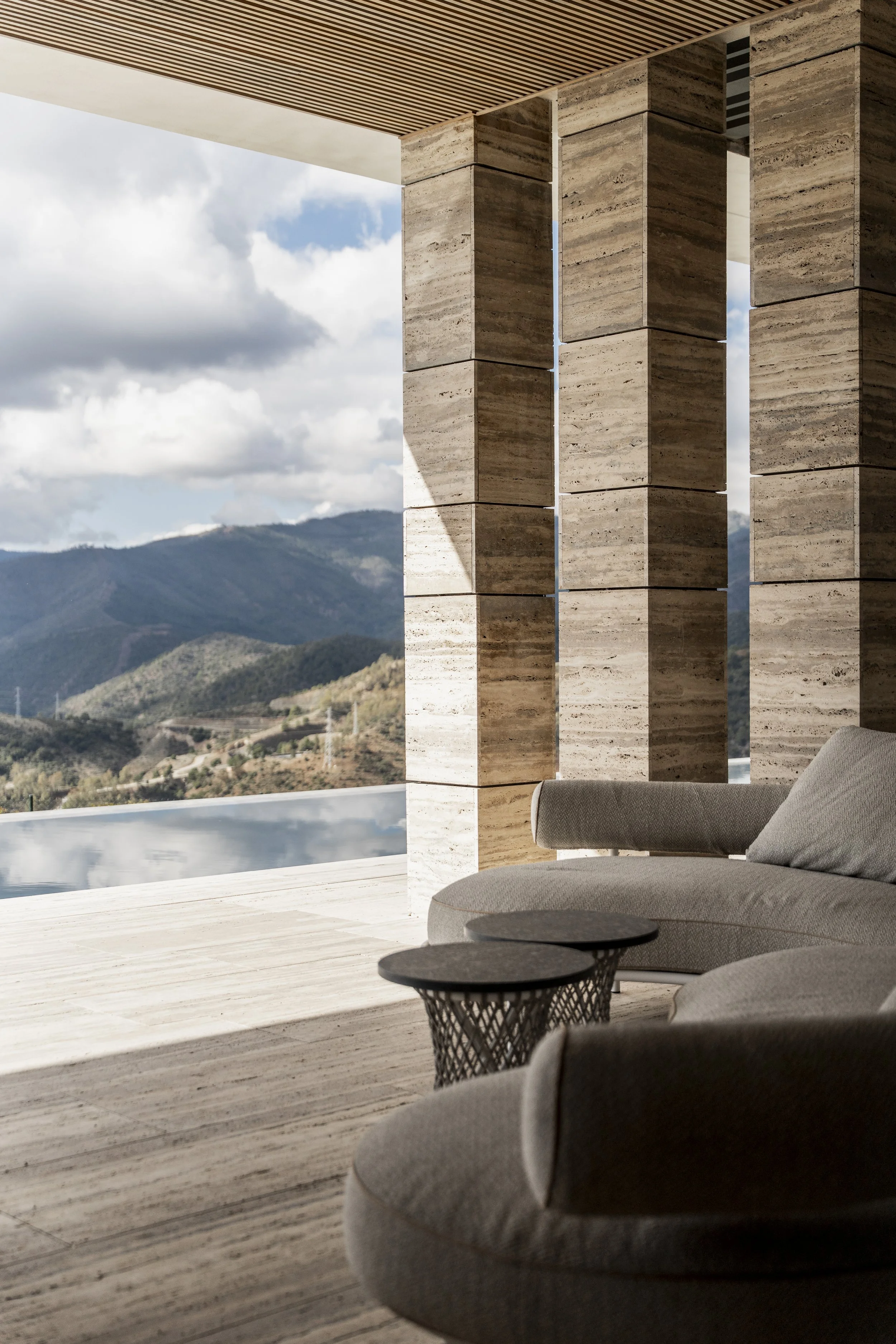 Sala moderna con sofá blanco, cojines decorativos, pared de madera con luces verticales y mesa con libros.
