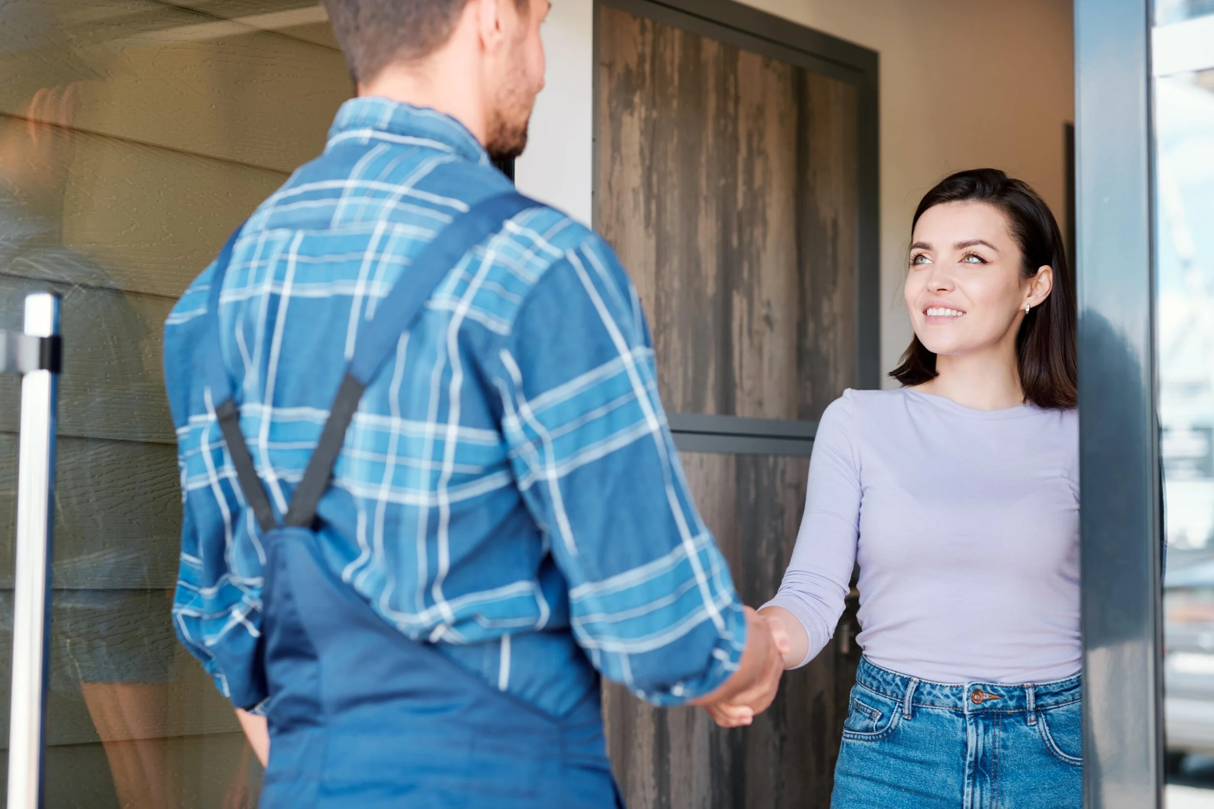A woman smiling and shaking hands with a technician at her front door.