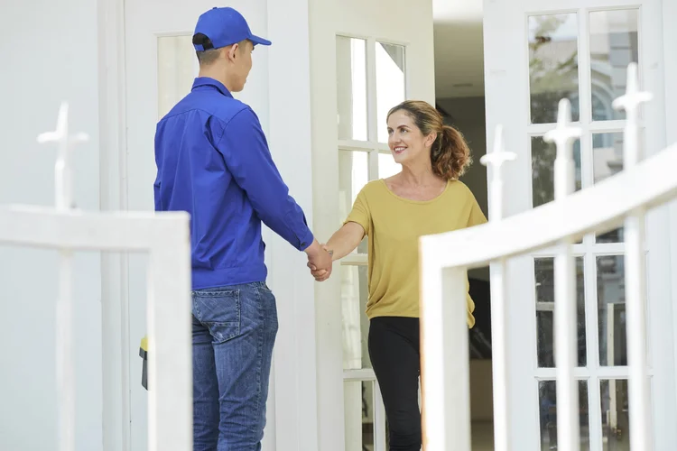 A woman smiling and shaking hands with a service technician at her door.