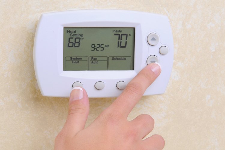 Finger pressing a button on a programmable wall thermostat