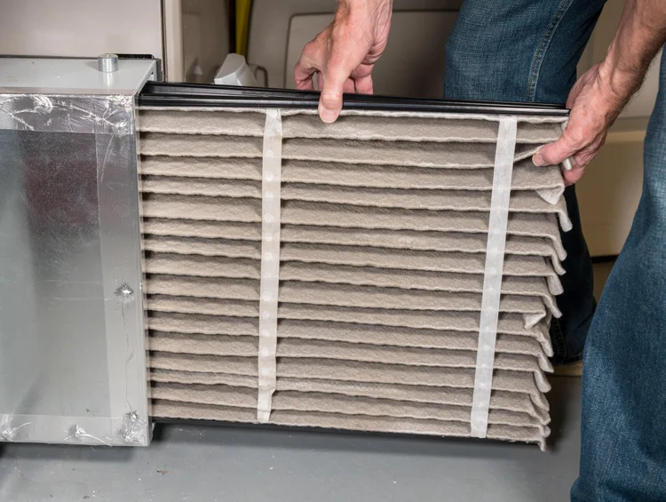 Dirty pleated furnace filter being pulled out of a furnace