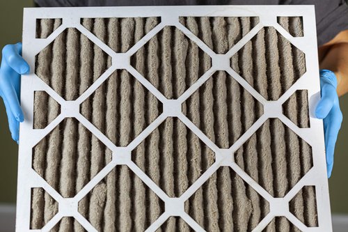 Dirty pleated furnace filter held in gloved hands