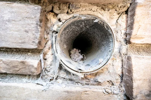 Exterior vent pipe through a stone wall with gaps around the opening