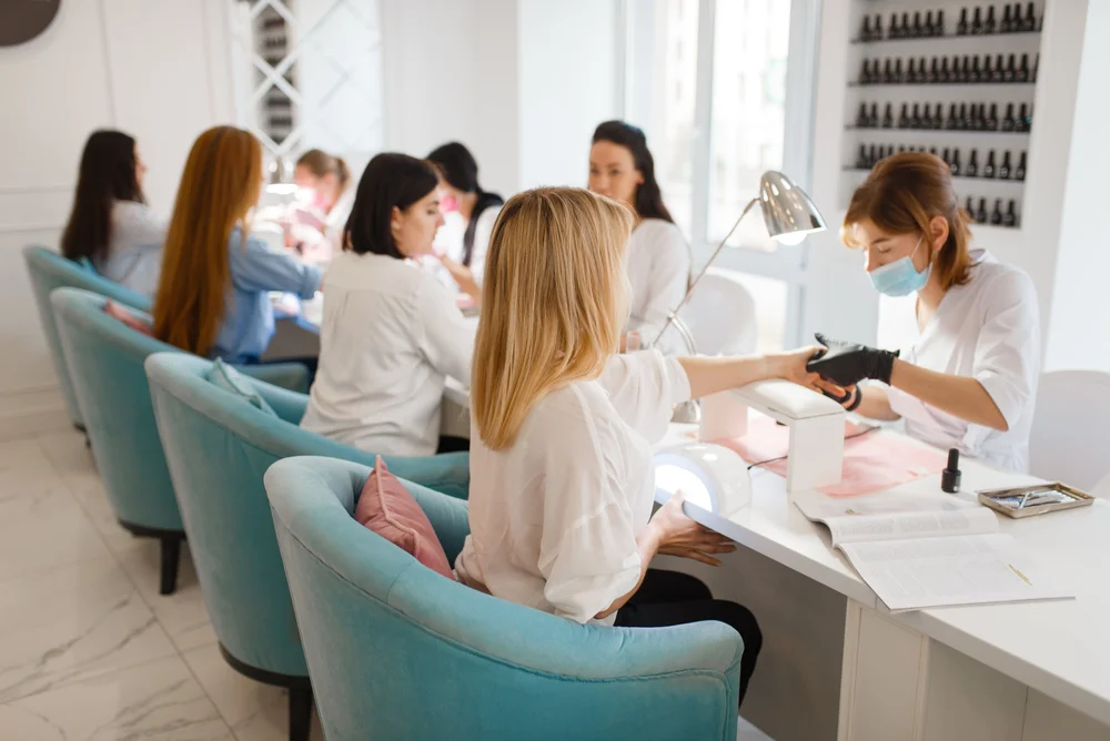 Nail technicians working with clients at a row of manicure tables in a nail salon