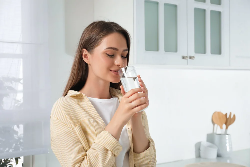 Woman drinking a glass of clear water in a bright white kitchen