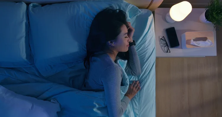A woman asleep in a dim, blue-lit bedroom