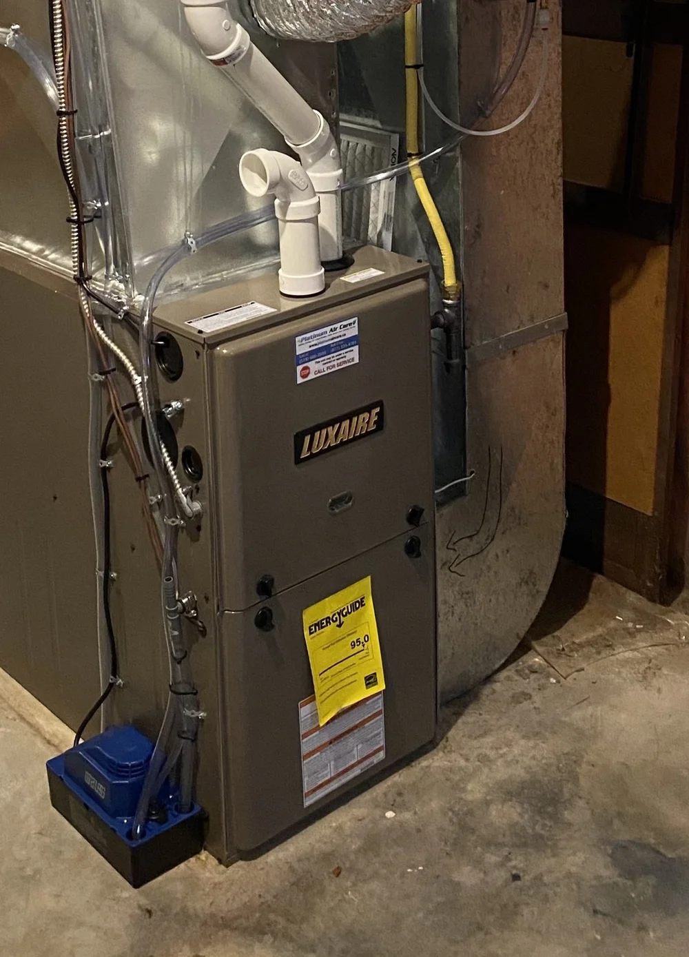 High-efficiency gas furnace with white PVC venting and a Platinum Air Care service sticker, in a home basement
