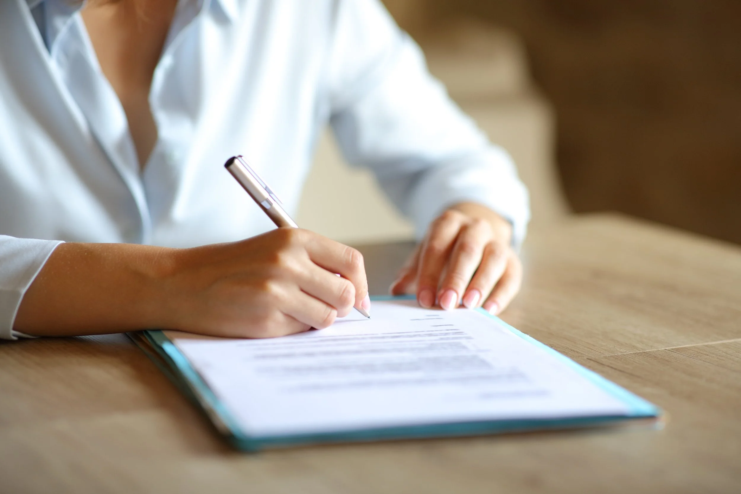 A person in a white shirt signing a document on a wooden table.