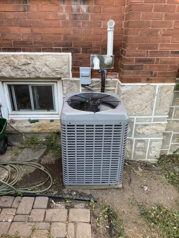 New central air conditioner condenser on a level pad beside a brick home